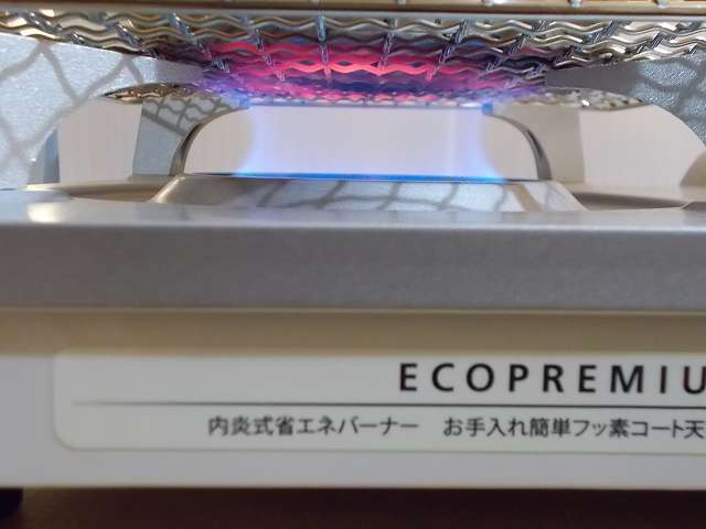 イワタニ カセットフー エコプレミアム CB-ECO-PRW の五徳（ごとく）にユニフレーム ネイチャーストーブ焼き網 SUS210 21cm 角 材質：ステンレス鋼を置いて、その上に水を入れたステンレス鍋を置いた状態でガスコンロを着火・点火したところ、ガスの炎が鍋底の中心から外側に広がっているのが焼き網の色でわかる