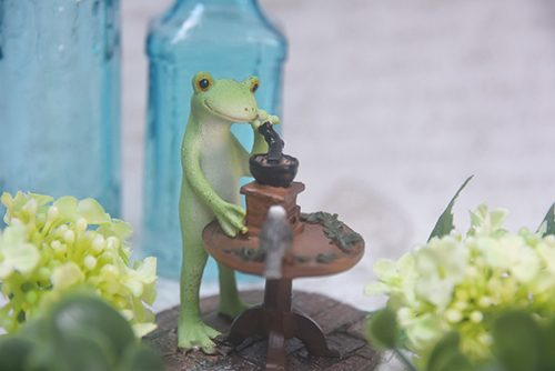 ツバキアキラが撮ったカエルのコポー。涼しげな青い瓶の前で珈琲を挽くコポー。